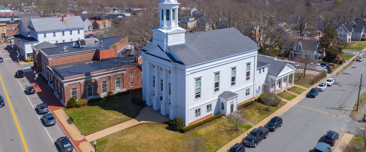 A church with a tall steeple, surrounded by residential buildings and a parking lot.