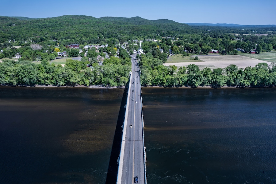 An aerial view of a bridge over a river with surrounding greenery and hills.