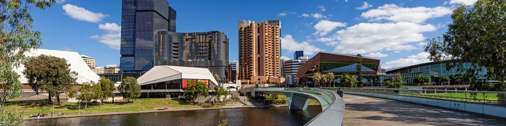 Um rio com uma ponte, edifícios modernos e um parque com árvores.