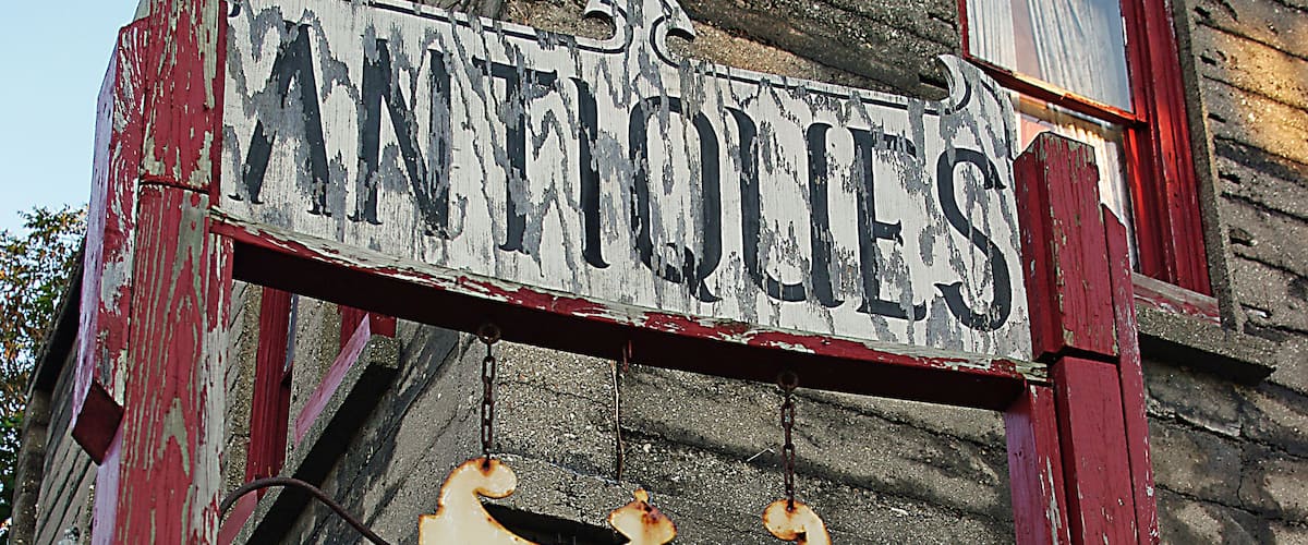 This antique sign is in front of a functioning antique store in a small town in the thumb area of Michigan.