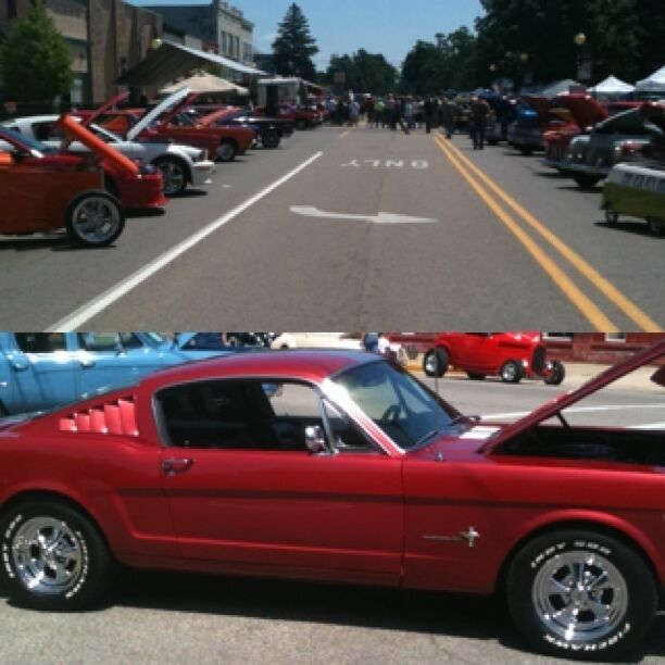 A red vintage car with its hood open, parked on a street with other vintage cars and a crowd of people.