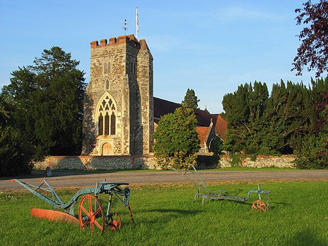 Waltham St Lawrence, Berkshire: west tower and Decorated Gothic west window of the Church of England parish church St Lawrence. There is old farm machinery at Church Farm in the foreground.