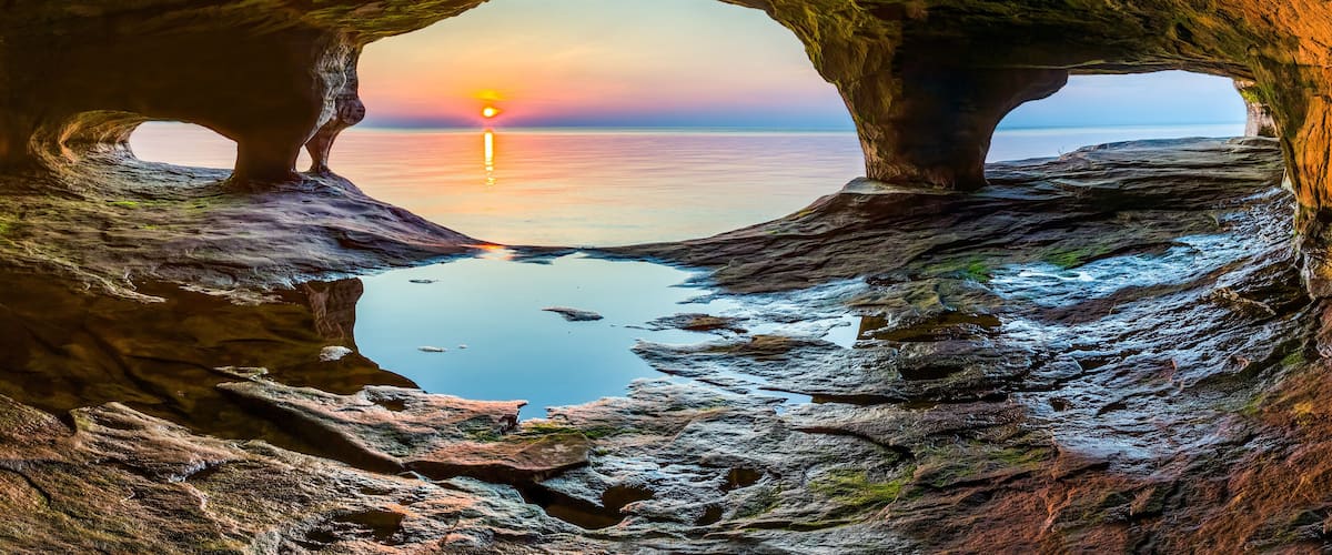 A cave opening to a sunset over a calm sea.