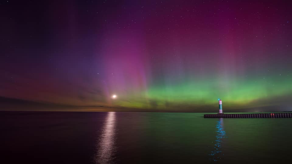 A lighthouse at night with the Northern Lights in the background.