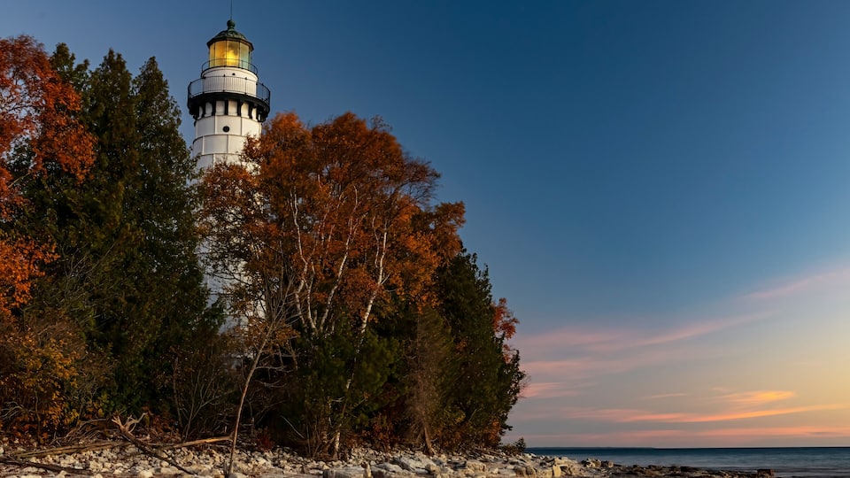 A lighthouse surrounded by autumn trees and rocky shoreline.
