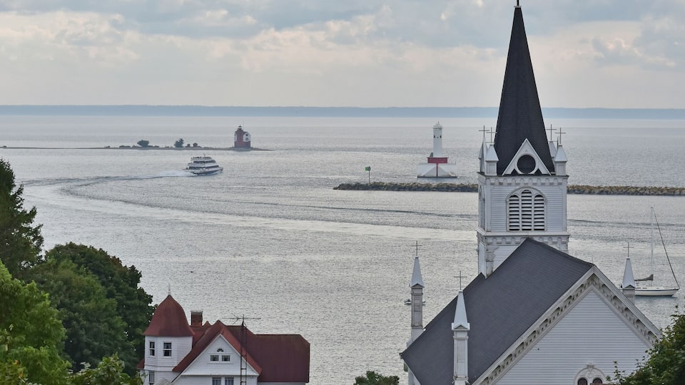 A church with a tall steeple and a cross, surrounded by greenery and a body of water with boats.