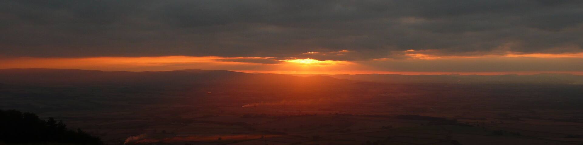 A sunset over a rural landscape with fields and a cloudy sky.
