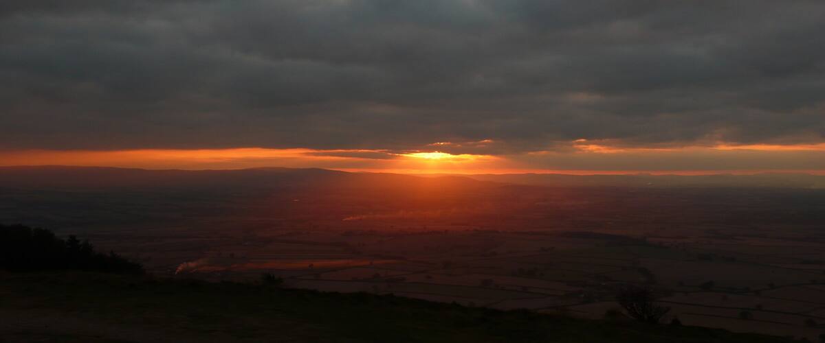 A sunset over a rural landscape with fields and a cloudy sky.