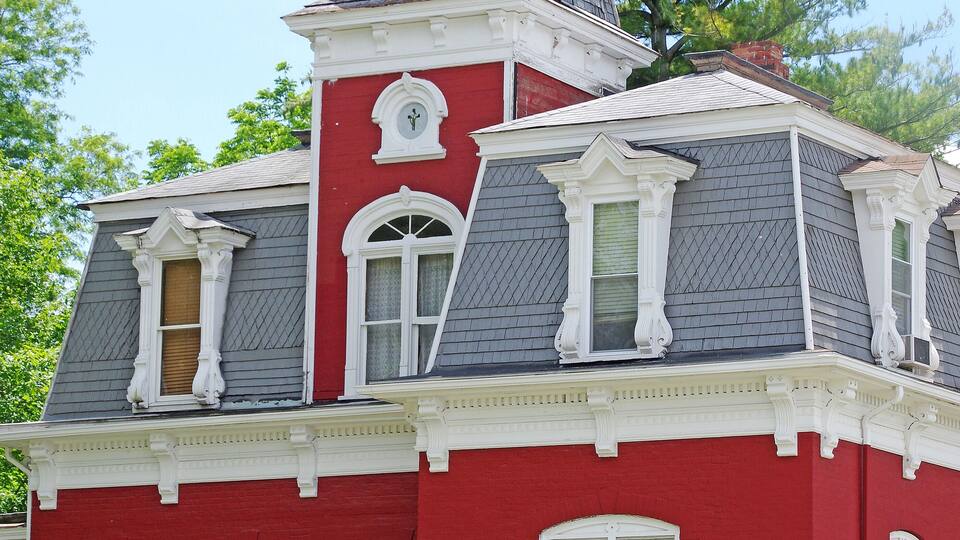 A red and white Victorian-style house with a prominent tower and a well-maintained front yard.