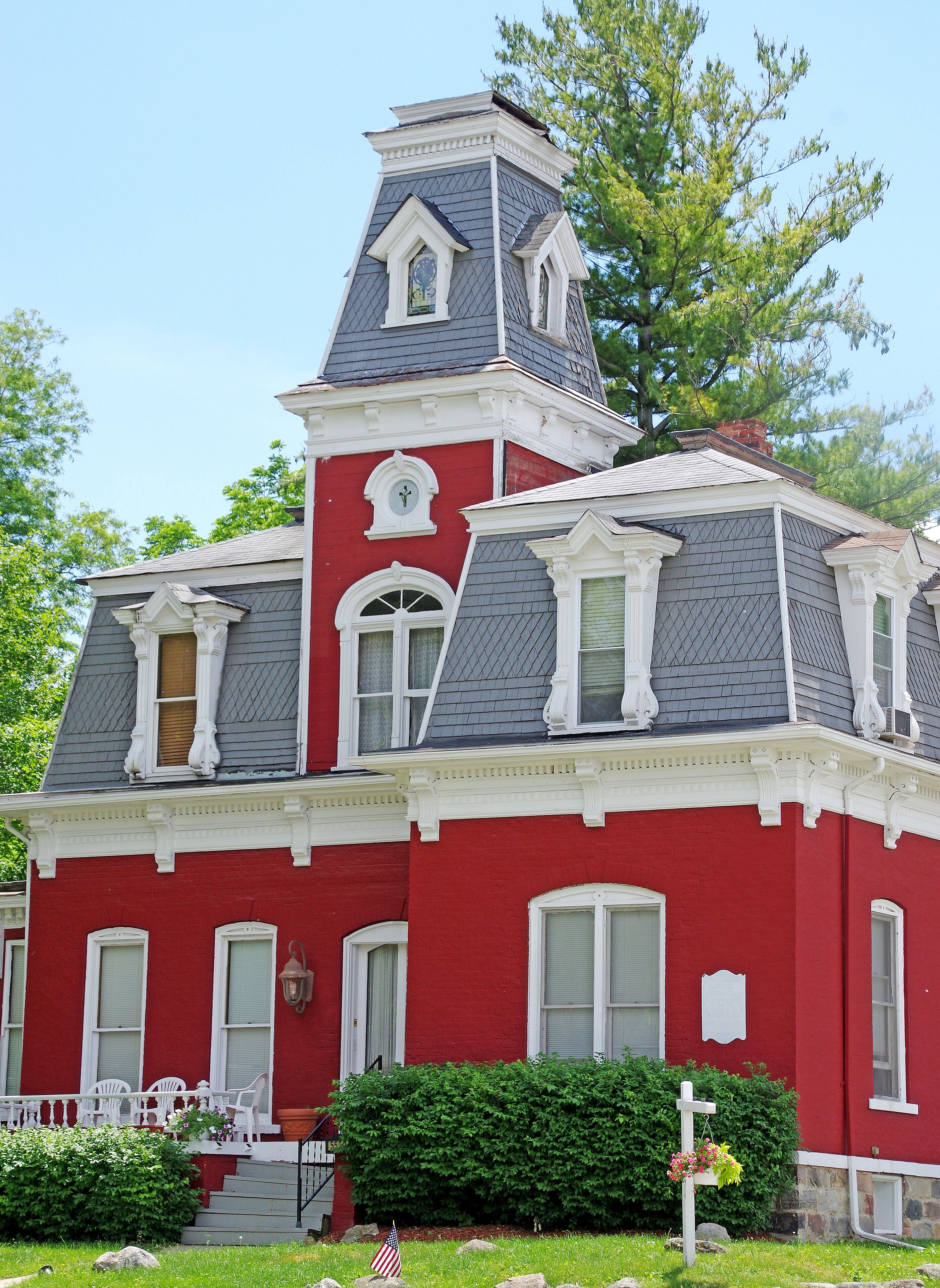 A red and white Victorian-style house with a prominent tower and a well-maintained front yard.