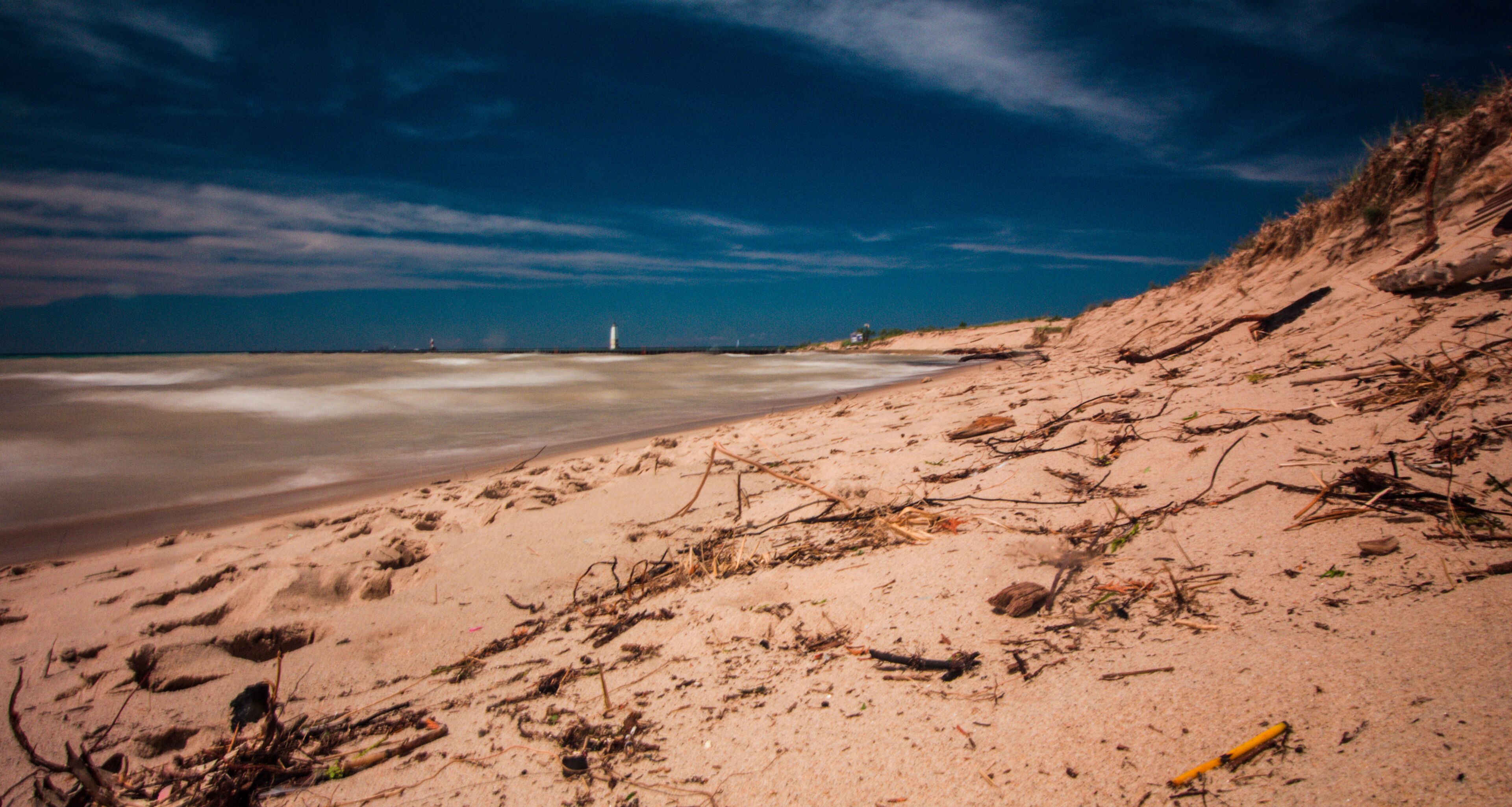 A sandy beach with scattered driftwood and a lighthouse in the distance.