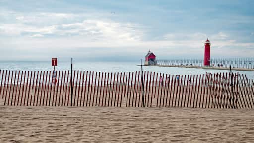 A family, just visible through fence slats, enjoys a walk on the beach, at Grand Haven, MI, lighthouse and pier in background.