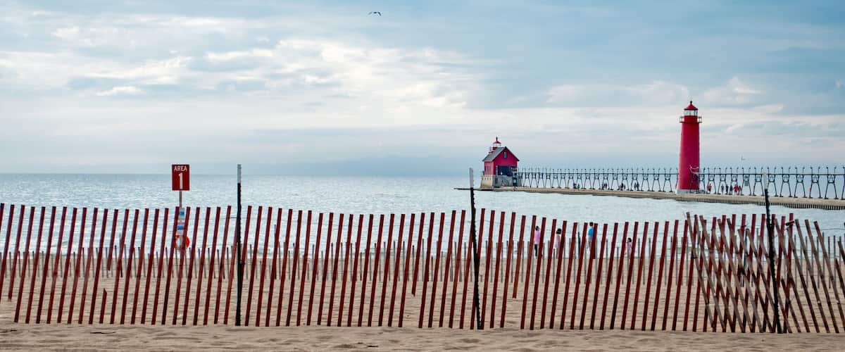 A beach with a wooden fence, a red lighthouse, and a pier with a small house.