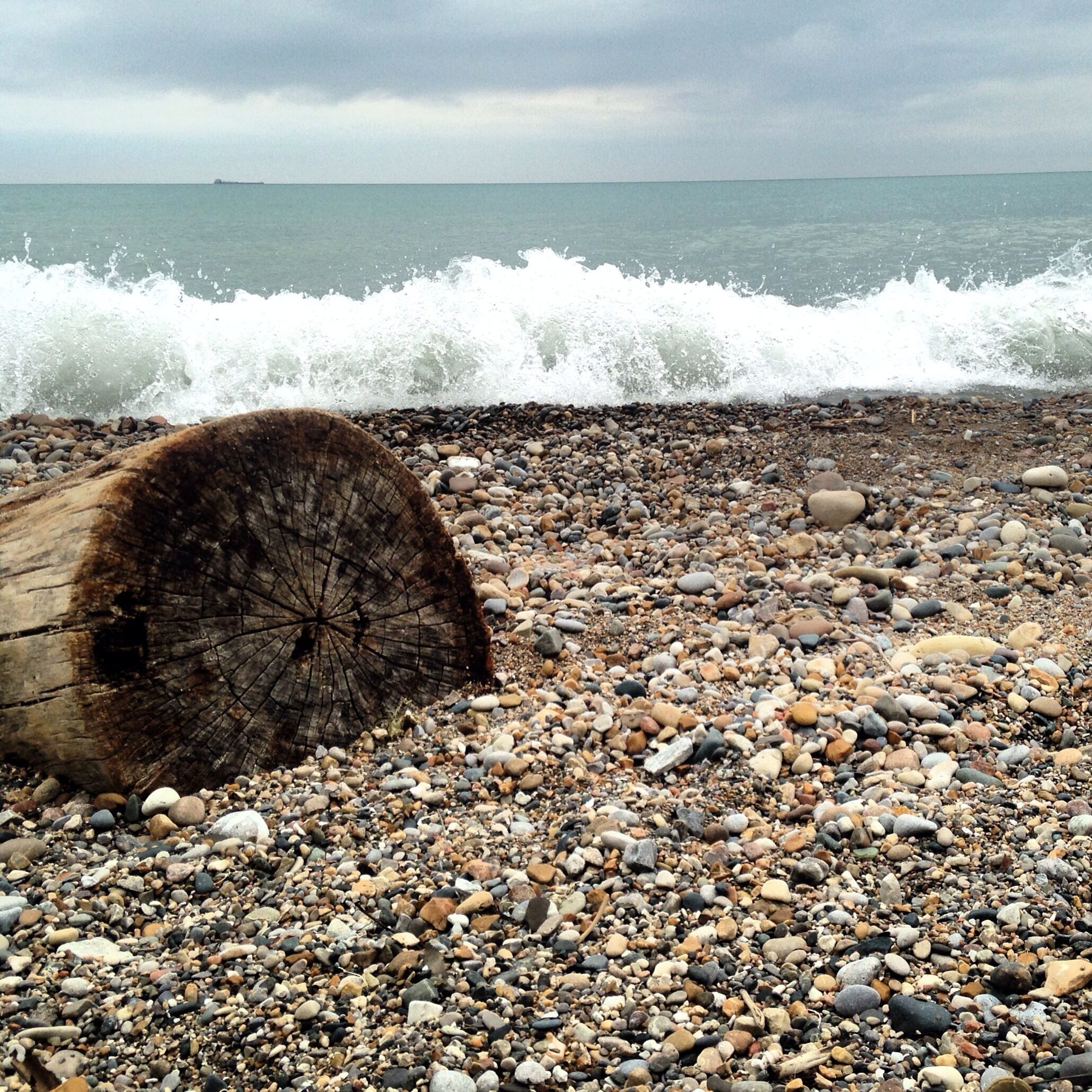 A rocky beach with a large log and waves crashing onto the shore.