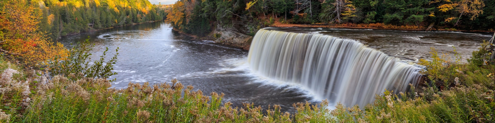 Une cascade située dans une zone boisée, avec un feuillage d’automne.