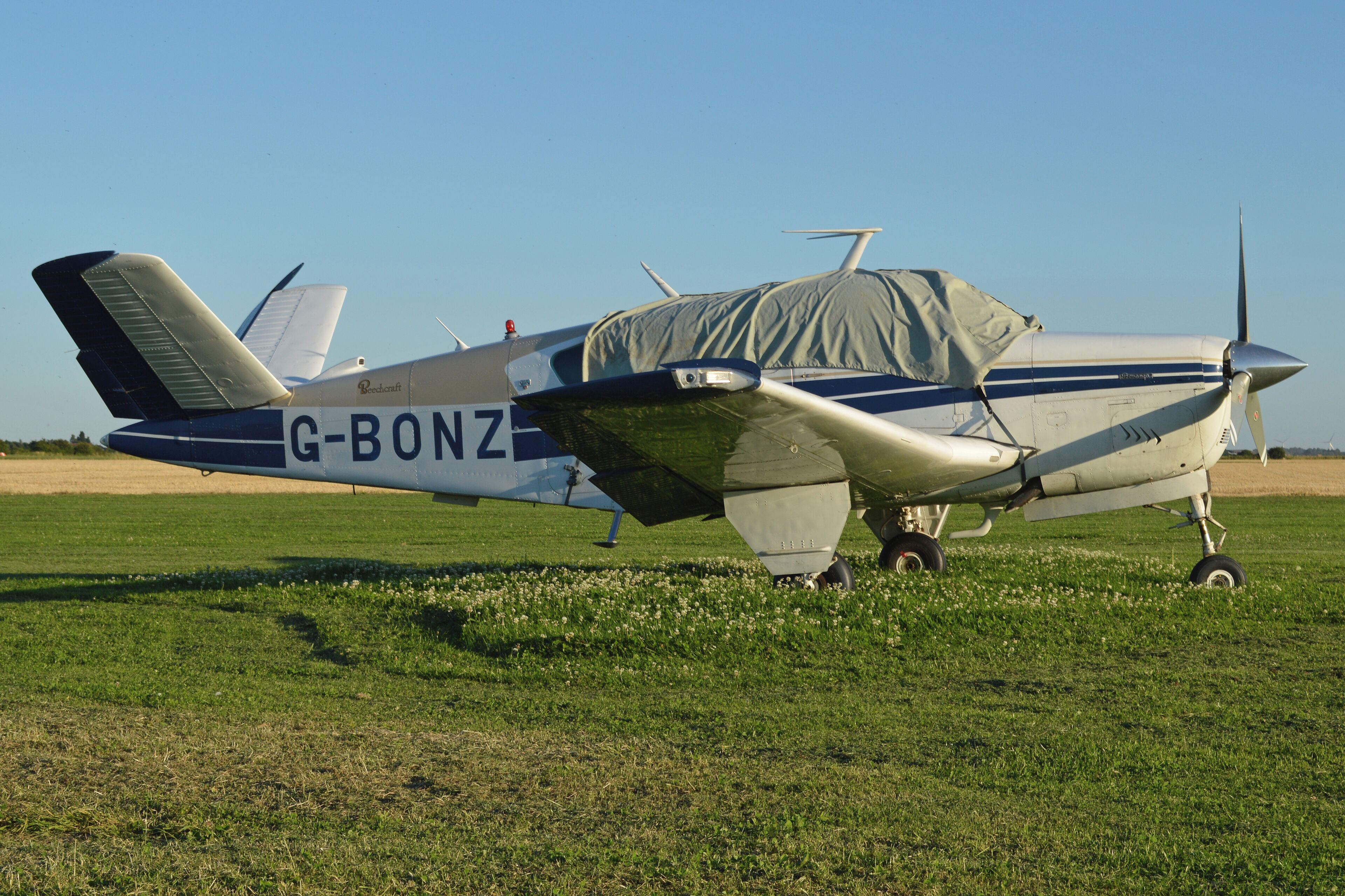 A small propeller plane with the registration G-BONZ parked on a grassy field.