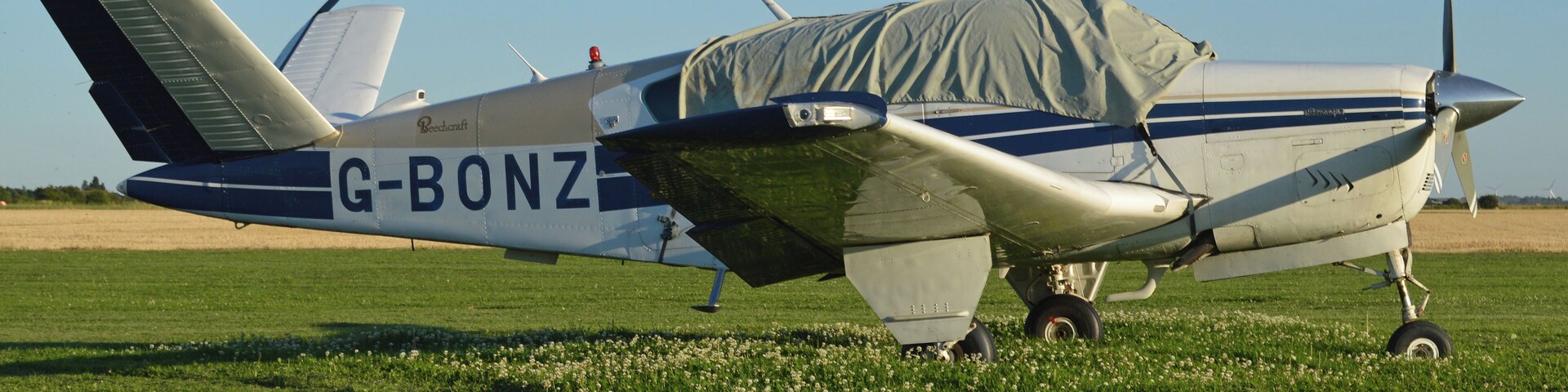 A small propeller plane with the registration G-BONZ parked on a grassy field.