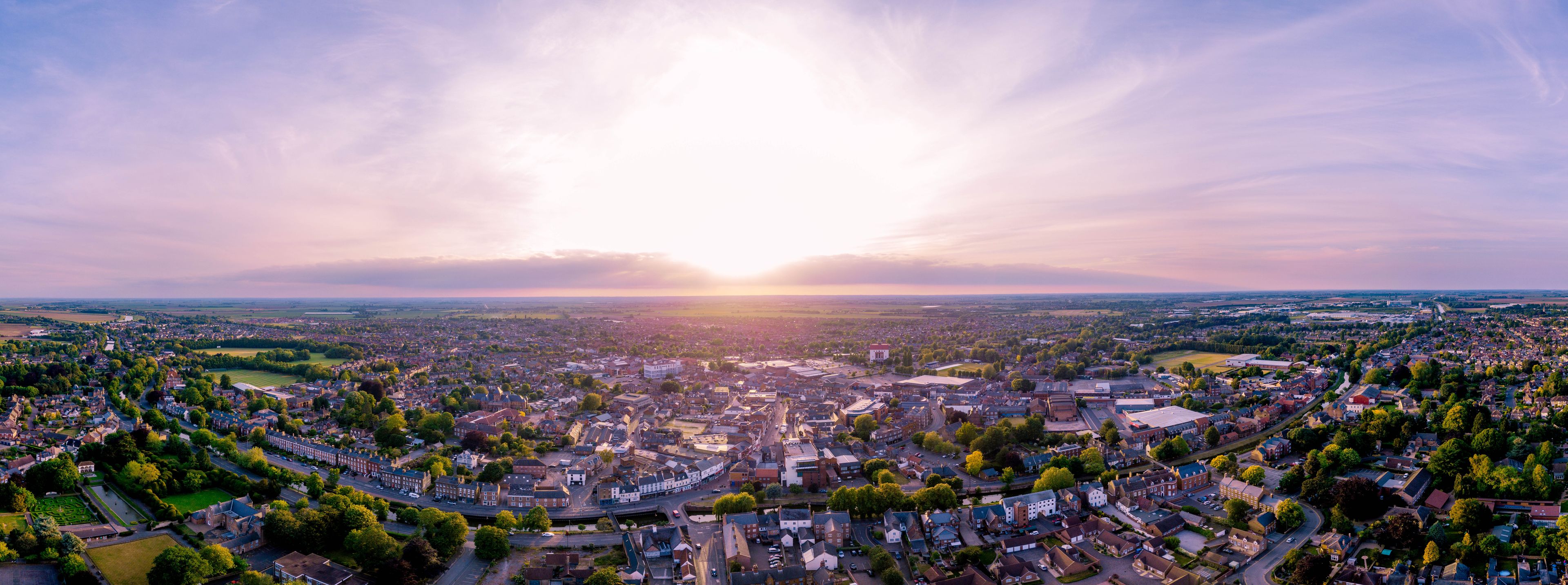 Ein Panoramablick auf eine Stadt bei Sonnenuntergang, wobei die Sonne am Himmel deutlich zu sehen ist.