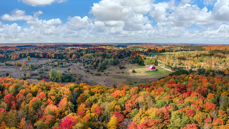 A rural landscape with a red barn, autumn foliage, and a clear sky.