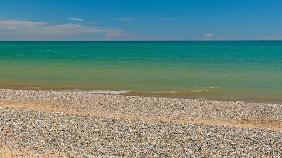 A pebbly beach with clear turquoise water and a clear sky.