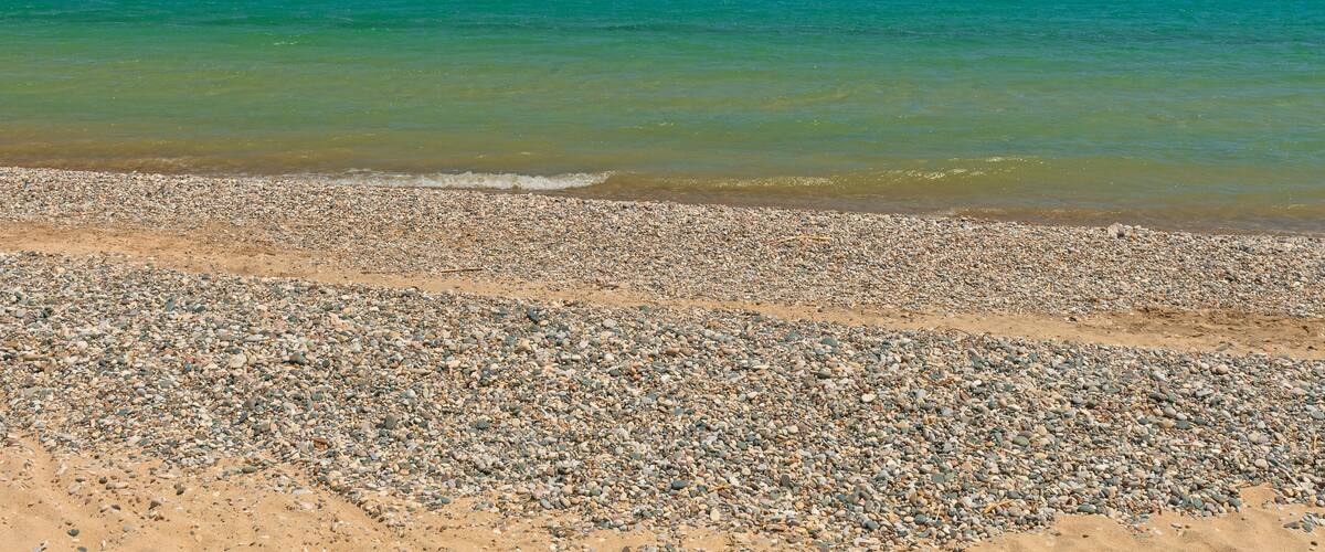 A pebbly beach with clear turquoise water and a clear sky.