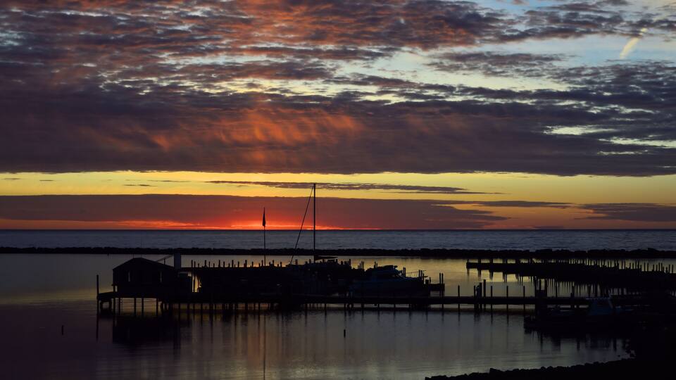 A sunset over a calm sea with a pier and a small building.