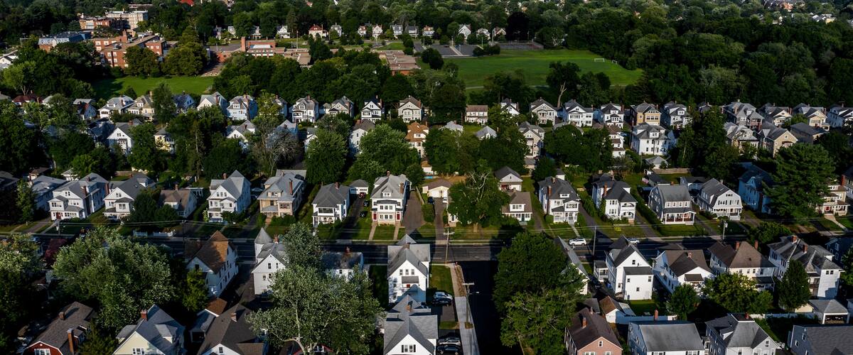 An aerial view of a residential area with houses, green spaces, and a distant city skyline.