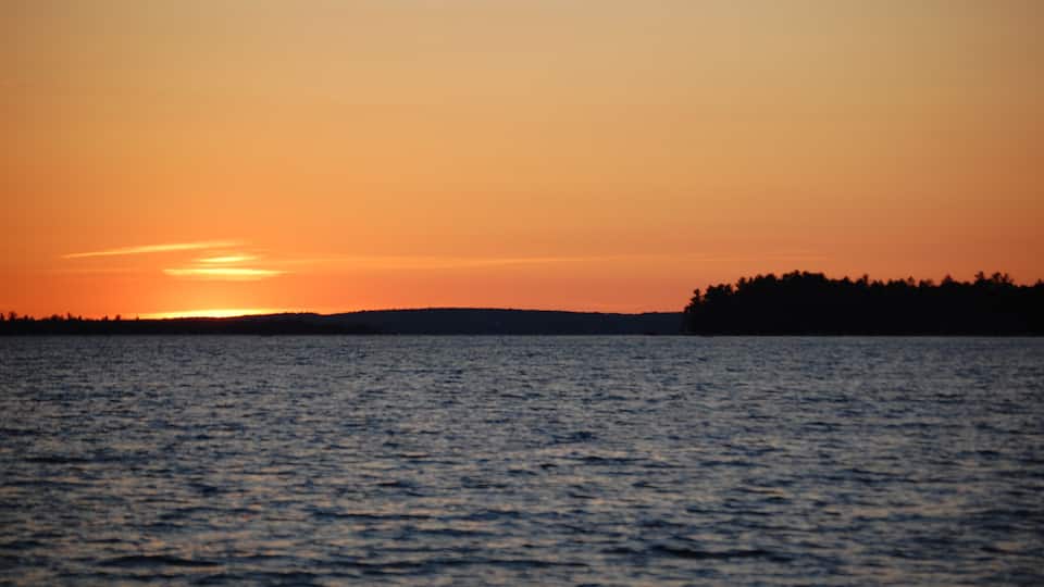 A sunset over a body of water with a silhouette of a forested landmass on the right.