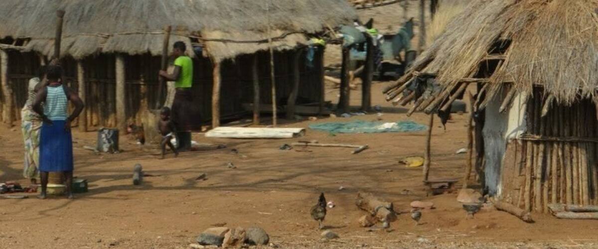 A rural village with thatched-roof huts, people engaged in daily activities, and chickens on the ground.