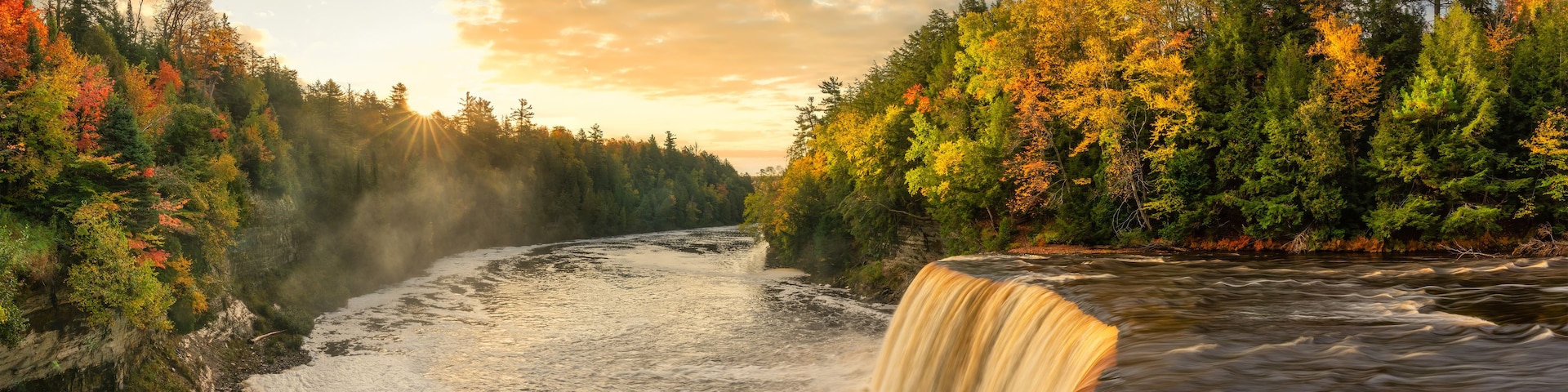 A waterfall cascading into a river surrounded by autumn-colored trees.