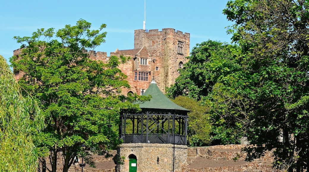 A stone structure with a green roof, a small pond, and a large castle in the background.