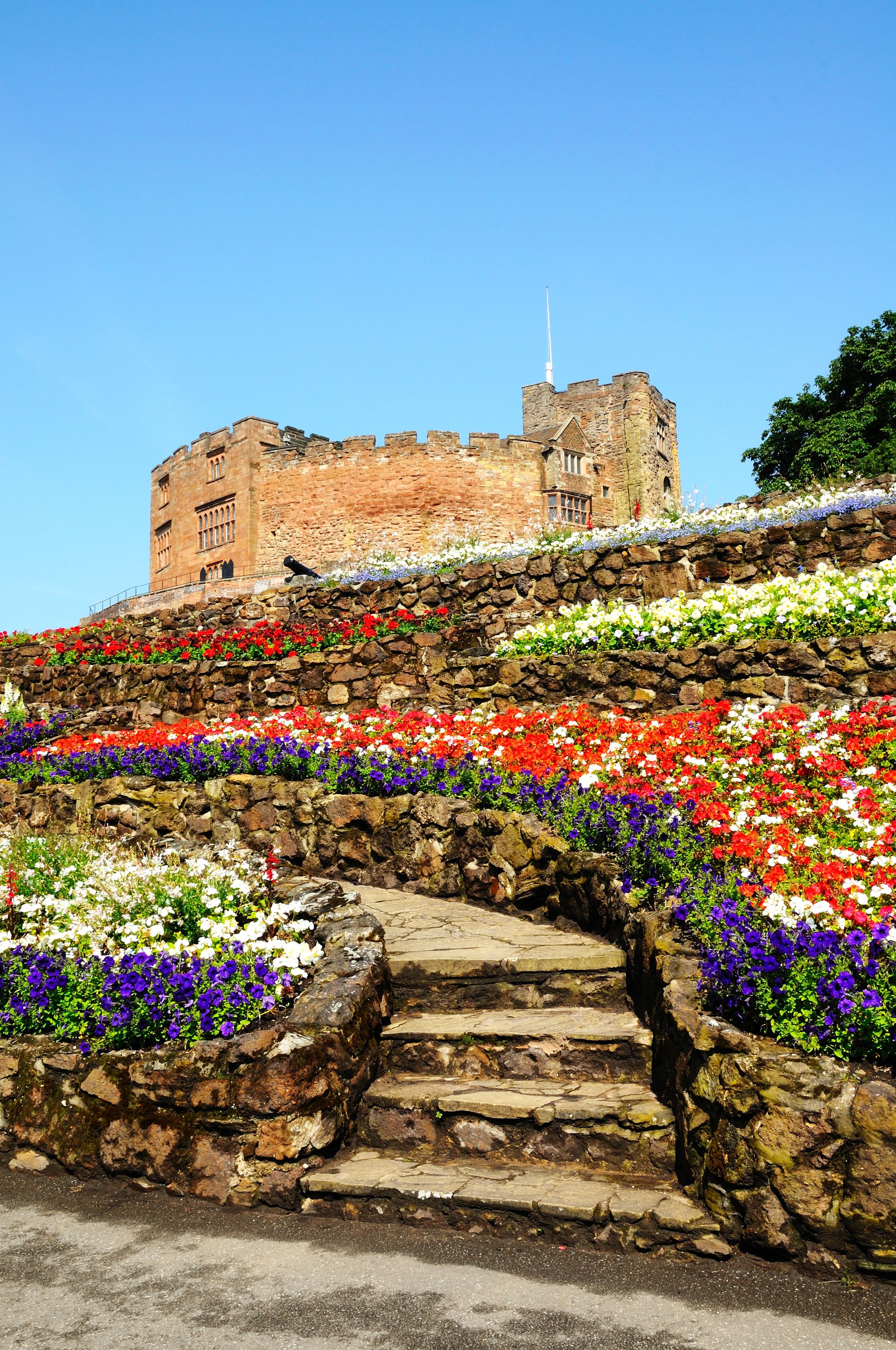 Un château doté d’un escalier en pierre, entouré de parterres de fleurs aux couleurs vives.