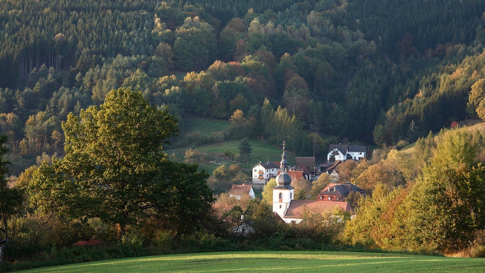 A rural landscape with a church, houses, and a forested hill.