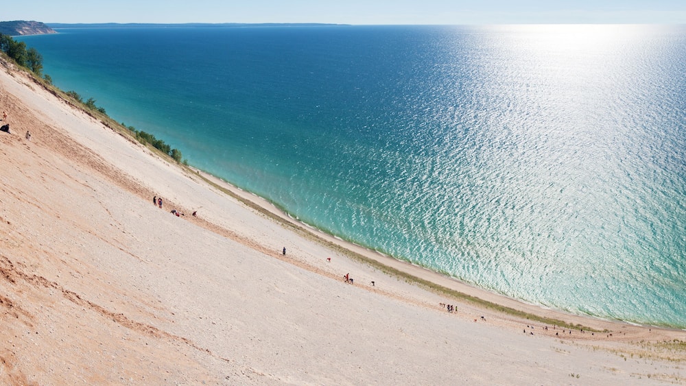 A sandy beach with clear turquoise water and a gentle slope leading to the sea.