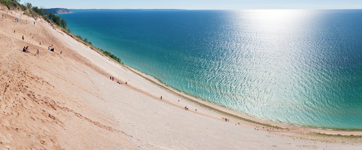 A sandy beach with clear turquoise water and a gentle slope leading to the sea.