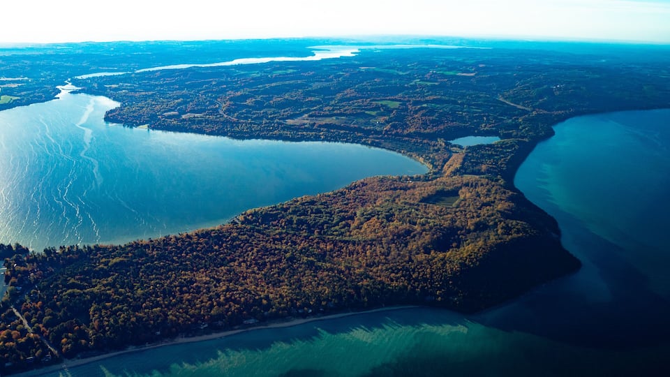 An aerial view of a coastal landscape with a large body of water, dense forested areas, and a winding road.