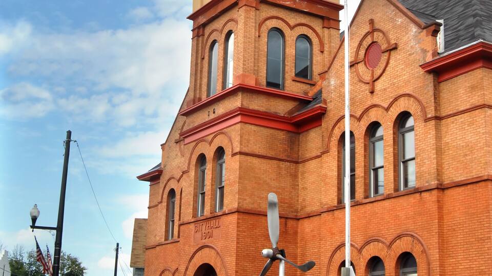A red brick building with a clock tower, American flags, and a sign reading 'City Hall 1901.'