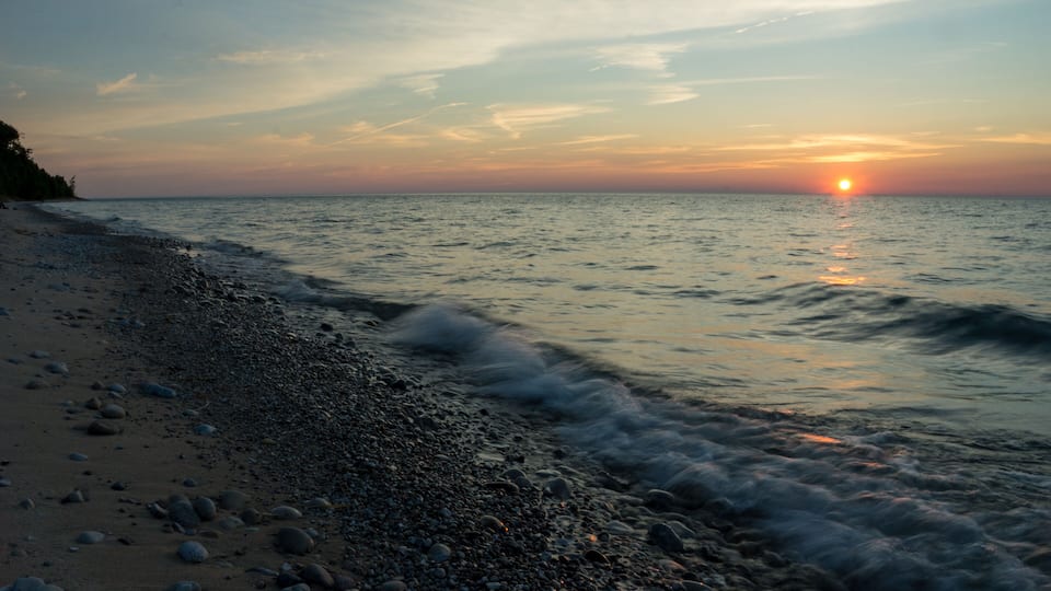A beach with pebbles and waves at sunset.