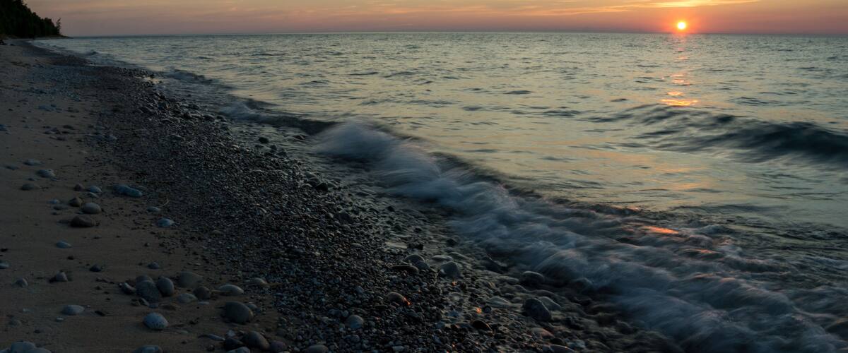 A beach with pebbles and waves at sunset.