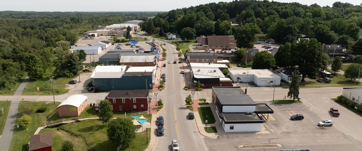 An aerial view of a small town with a main road, industrial buildings, and surrounding greenery.