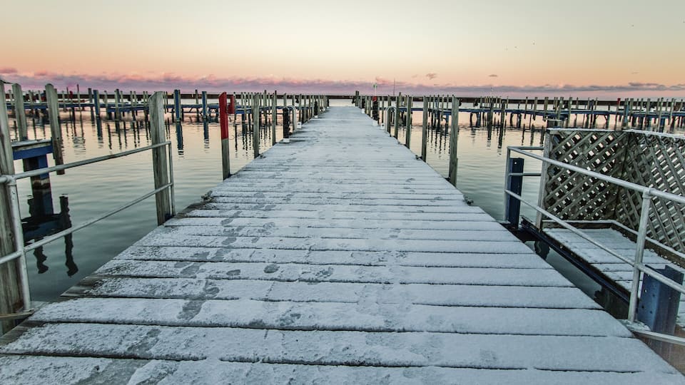 A wooden pier extending into calm water with a sunset in the background.