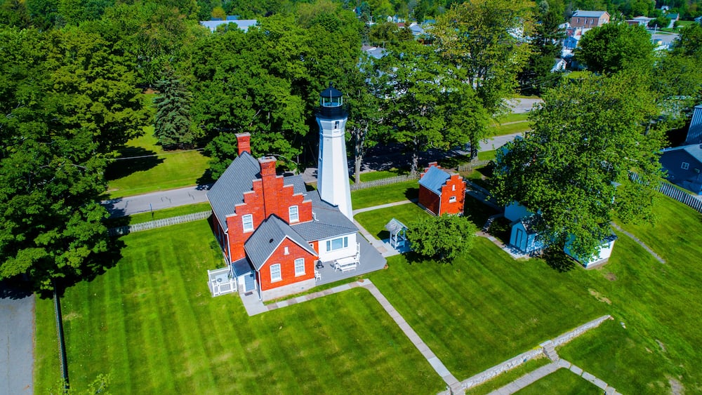 An aerial view of a residential area with a prominent lighthouse, red and white houses, and lush green lawns.