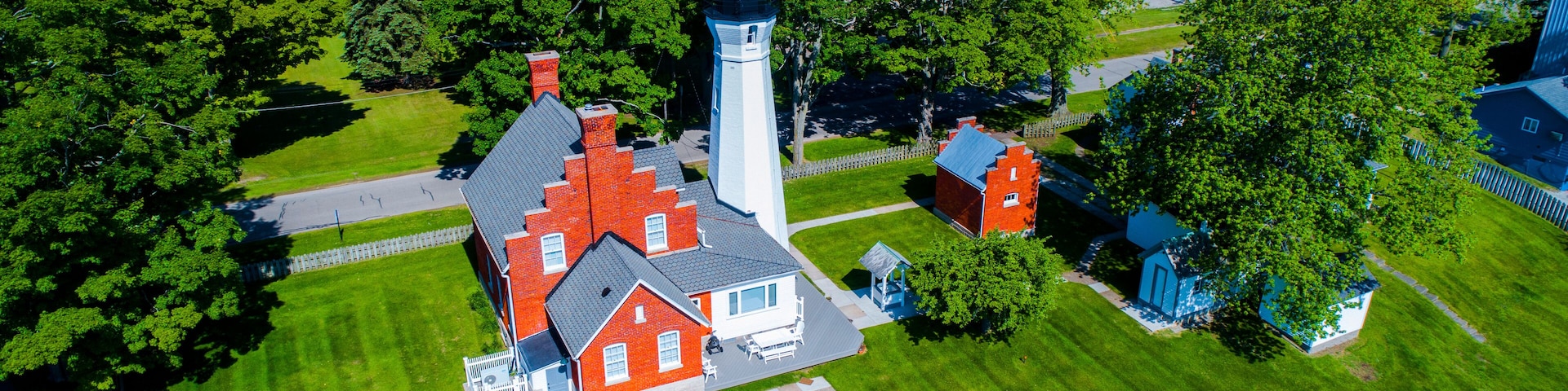 An aerial view of a residential area with a prominent lighthouse, red and white houses, and lush green lawns.