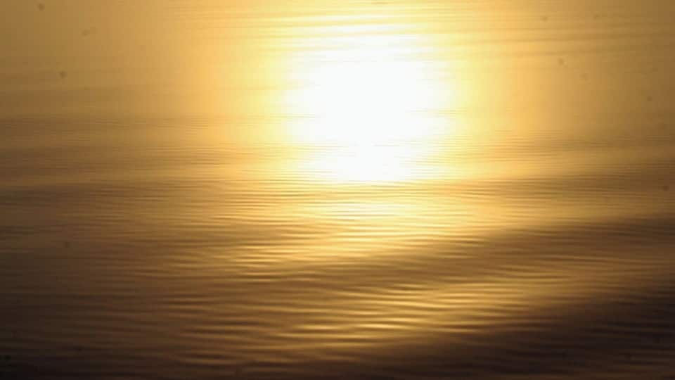 A boat on calm water with a bright sun in the background.
