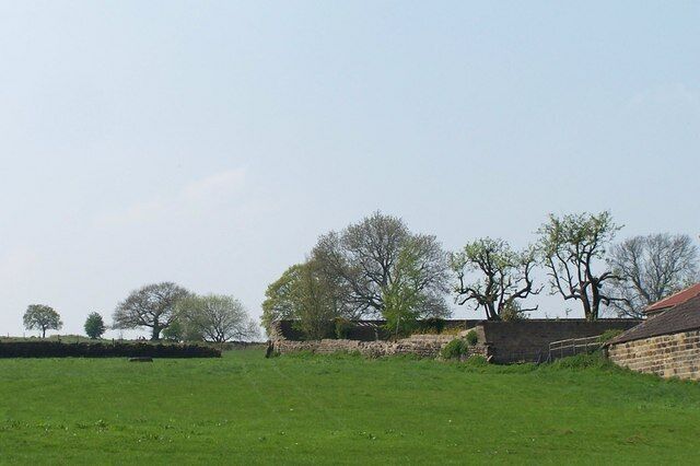 A rural landscape with a stone wall, a brick building, and trees.
