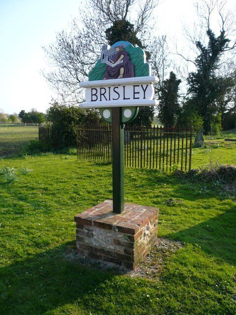 A signpost with the name 'BRISLEY' and a decorative emblem.