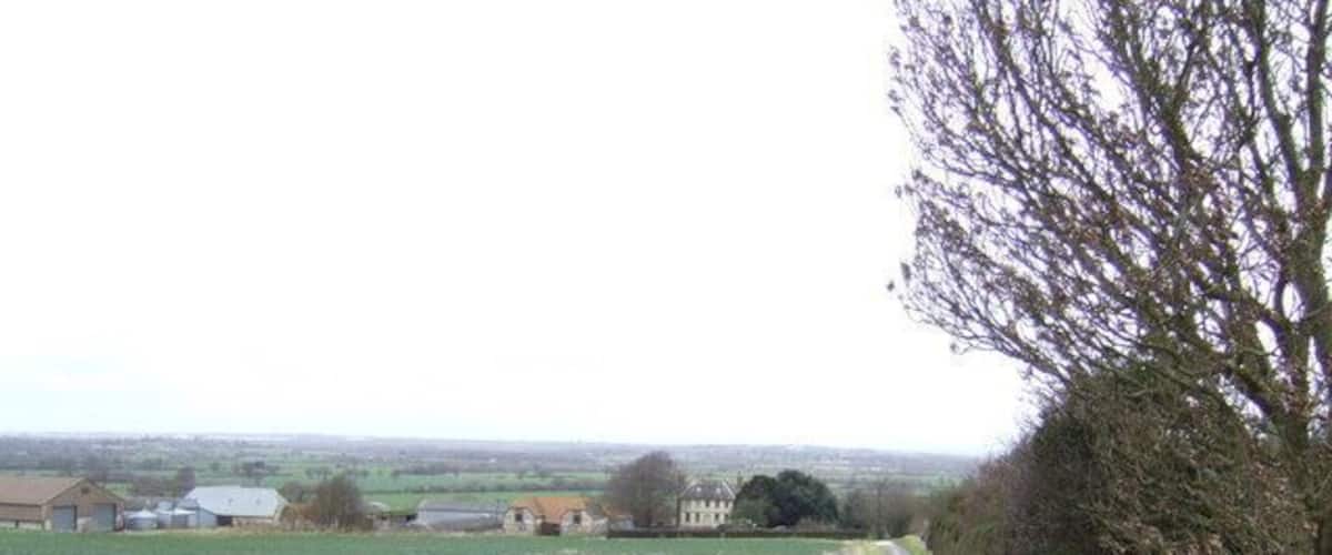 A rural road curving through fields with farm buildings in the distance.