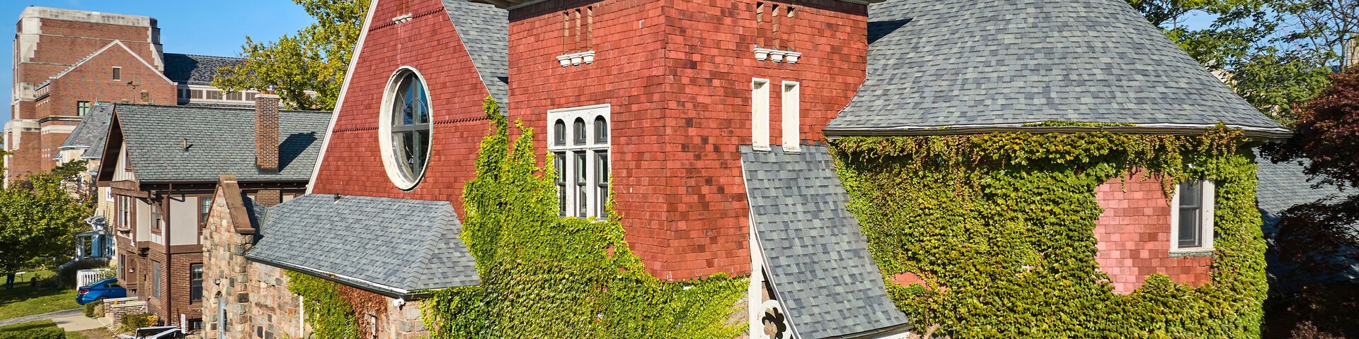 A red brick house with a steeply pitched roof and a green ivy-covered section.