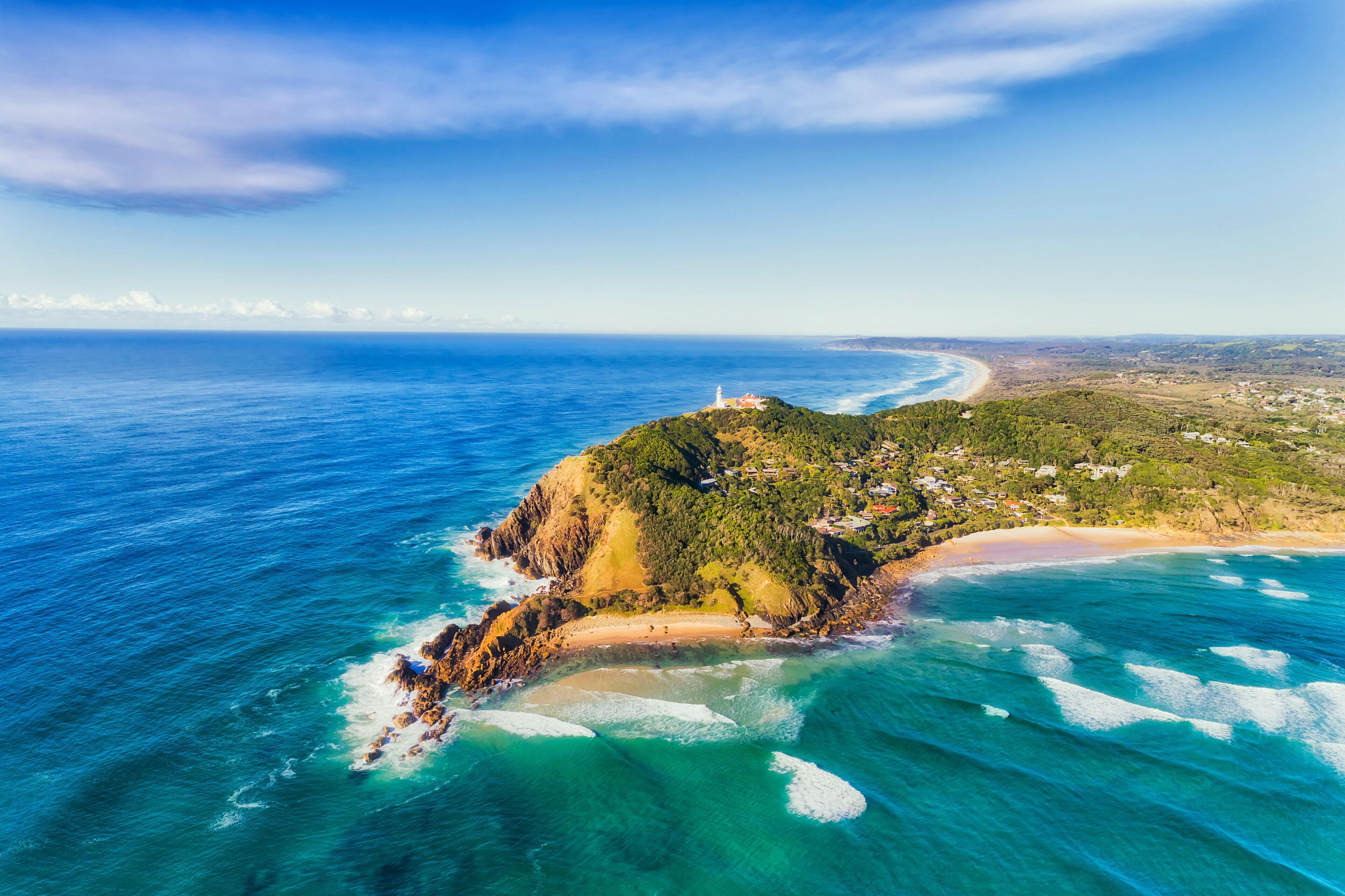 An aerial view of a coastal landscape with a lighthouse, a beach, and a small town.