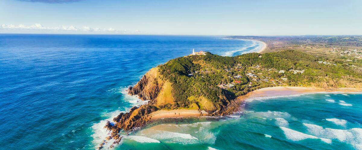 An aerial view of a coastal landscape with a lighthouse, a beach, and a small town.